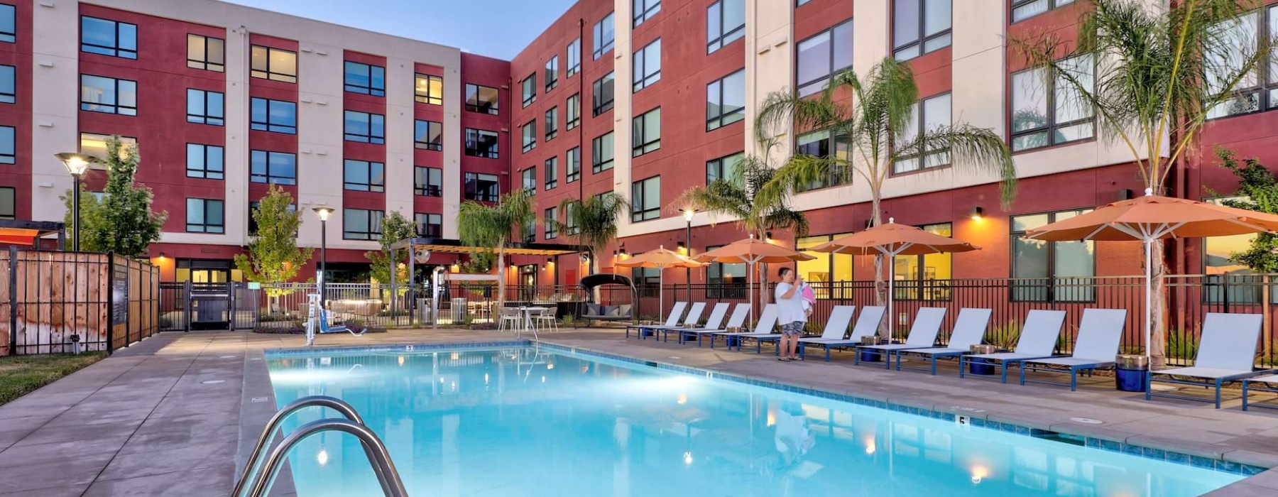 West Sacramento, CA Luxury Studio Apartments | The Bernice | Pool with Spacious Sun Deck, Lounge Chairs, Umbrellas, and Palm Trees.